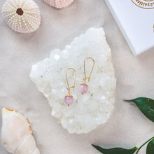 Ladda upp bild till gallerivisning, Elegant Kunzite earrings with details in 18k gold-plated 925 sterling silver. Presented on a crystal cluster on a beach.